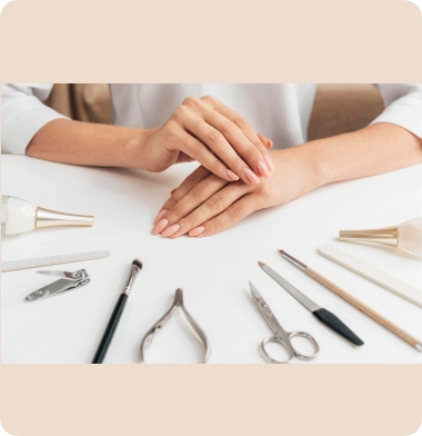 Des mains aux ongles manucurés reposent sur une table blanche entourée d'outils de manucure tels que des ciseaux, une lime, du vernis et un pinceau, créant une atmosphère soignée et élégante.